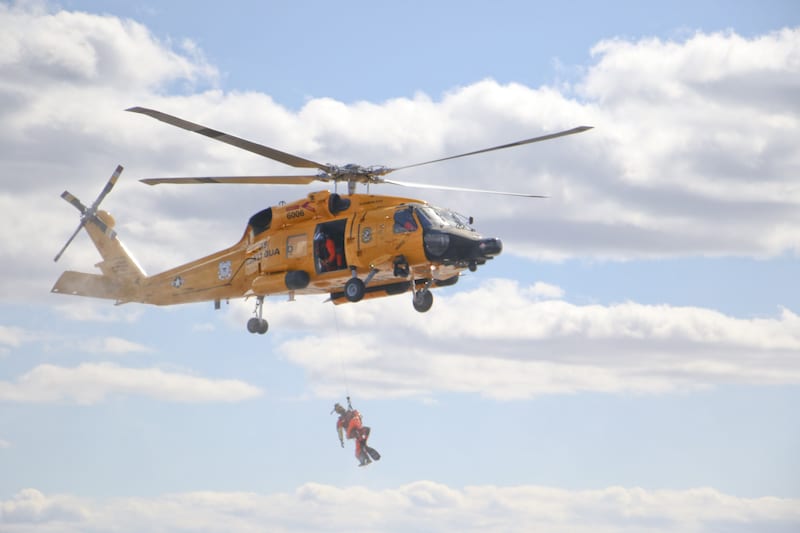 A rescue swimmer hangs below an MH-60 Medium Range Recovery Helicopter Friday, Feb. 26, 2016, during a search and rescue demonstration near Elizabeth City, N.C. U.S. Coast Guard helicopters were painted the retro color scheme to celebrate the Coast Guard's aviation centennial birthday. (U.S. Coast Guard photograph by Lt. Cmdr. Krystyn Pecora)