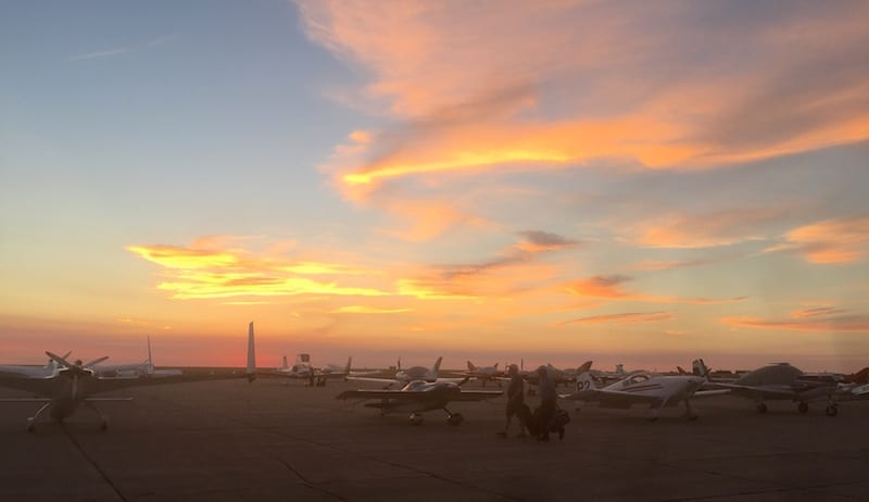 Racers make their way to their planes at dawn. The skies above the flight line before the start of the AirVenture Cup race suggested fine weather, but farther up the course conditions were IFR, prompting both a delay in launch and a mid-race stop for all 71 race planes at Owatonna, Illinois. (Photo by William E. Dubois)