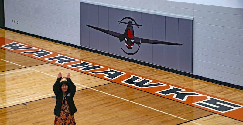 Ridgevue High principal Julie Yamamoto raises her hands to make the Warhawks 'W' sign in the gym where the namesake aircraft decorates the basketball court.