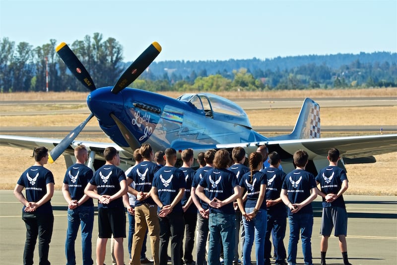 A group of new U.S. Air Force recruits prepares to take their Oath of Enlistment with a P-51 Mustang as a backdrop.