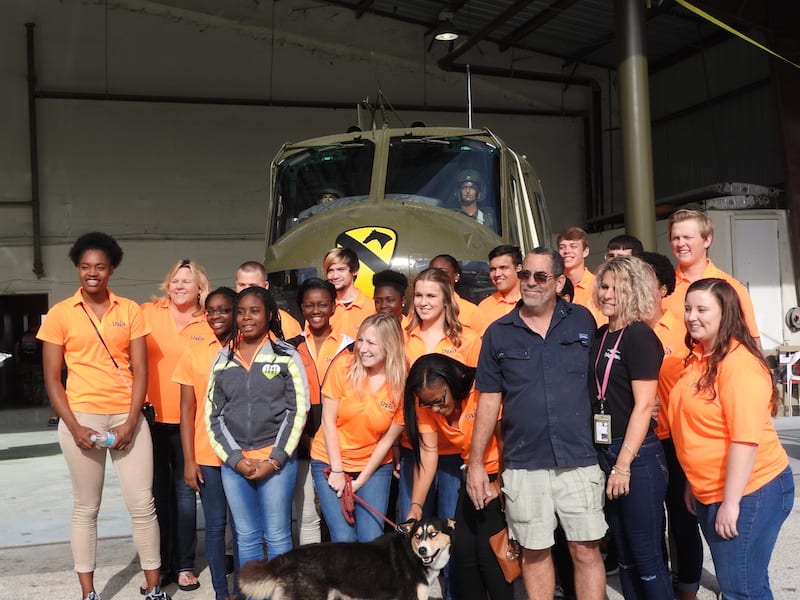 John and Mischele  Francis, owners of the Flying Colors Paint Shop, have their picture taken with the students in front of a recently painted Huey helicopter about to become a part of a Veterans Memorial on display in Leesburg, Florida.