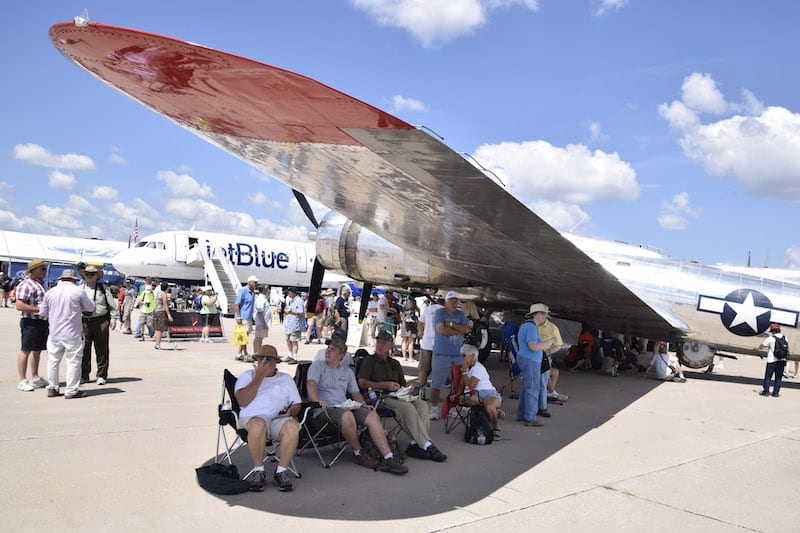 AirVenture visitors find a shady spot under the wing of the Yankee Lady, a B-17G on display at Air Venture 2016.